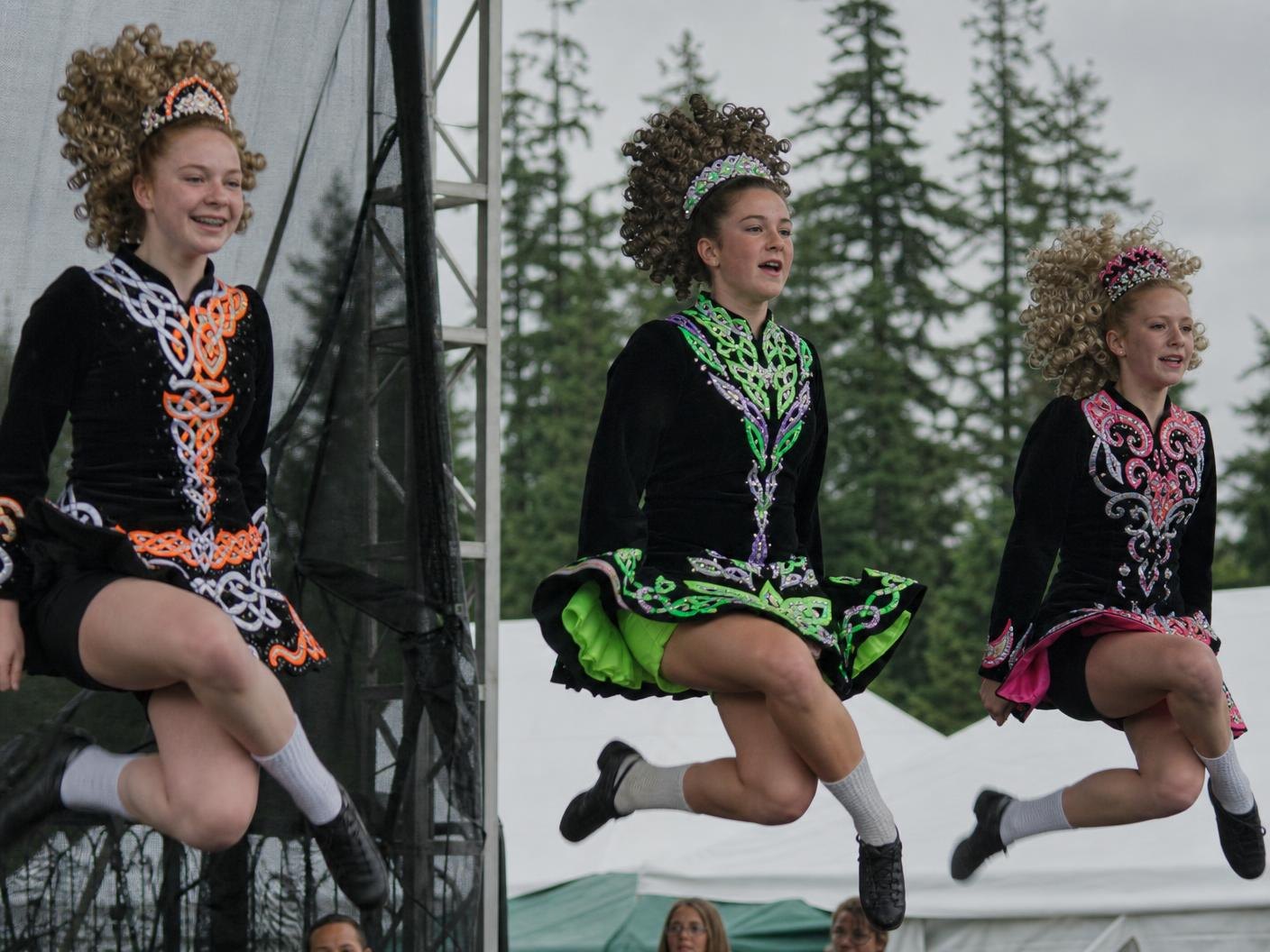 Three Irish step dancers in embroidered dresses caught mid-leap on an outdoor stage